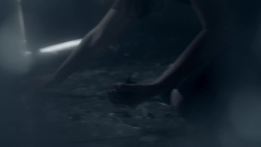 A person picks up glass from the floor of a dark room