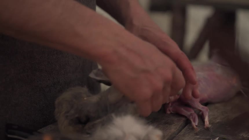 Hunter stands at a table in his camp and skins a rabbit
