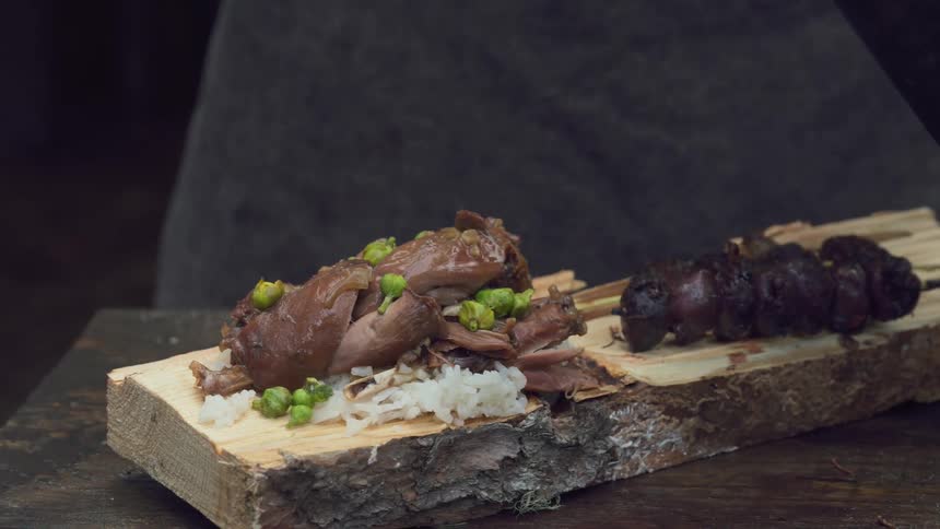 A beautifully plated dish of braised meat and grilled sausage served on a rustic wooden plank