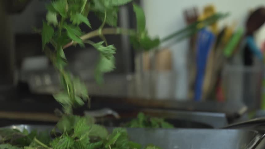 A chef moves some leafy greens from a metal pan to a skillet