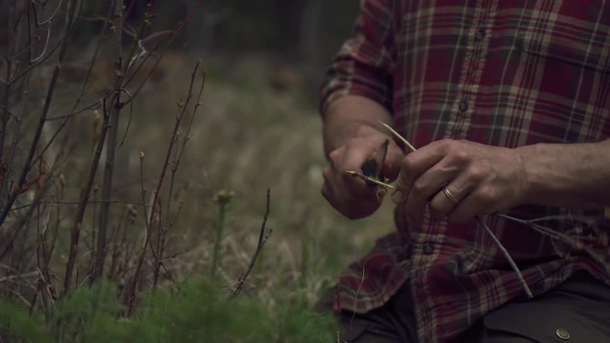 A man is shaving sticks with his knife