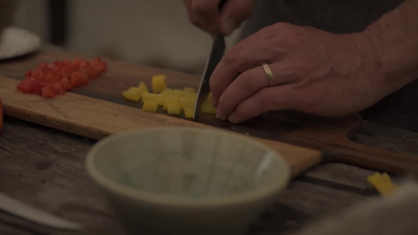 Mans hands slicing yellow bell peppers on a wooden cutting board