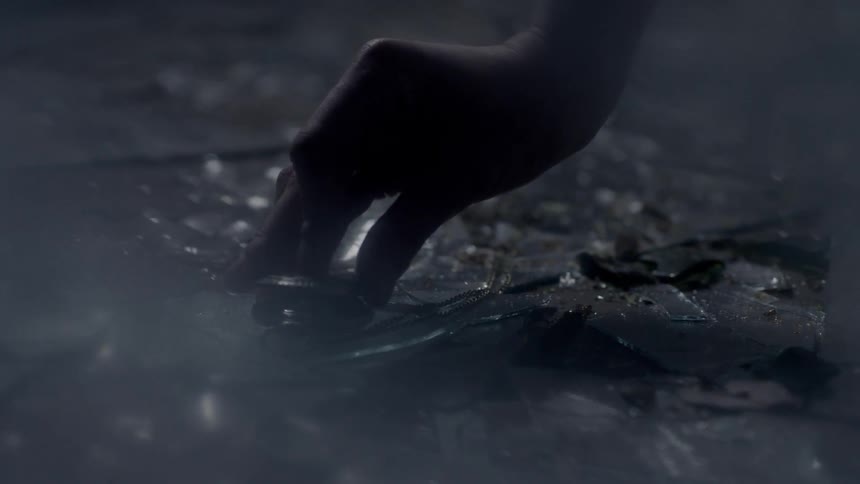 A female hand is reaching for and closing a broken pocket watch lying on a floor