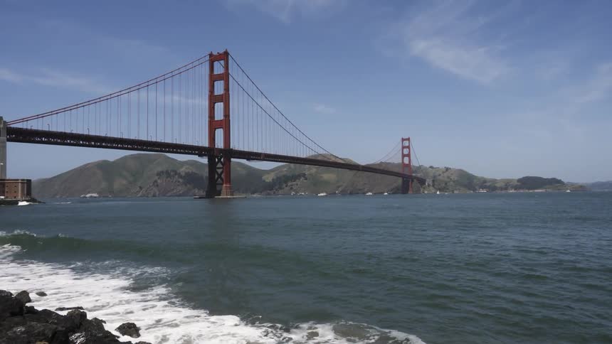 Waves crash against the shore by the large bridge