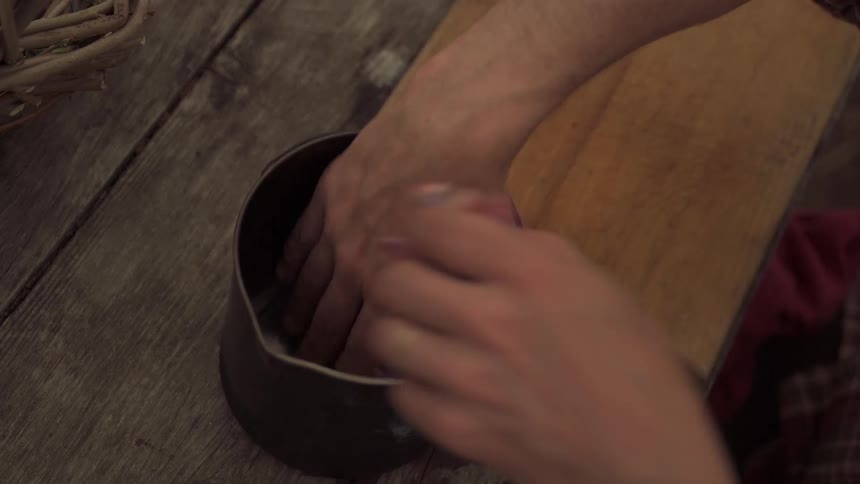 Closeup of a mans hands placing game meat into a pot on a wooden table in a rustic setting