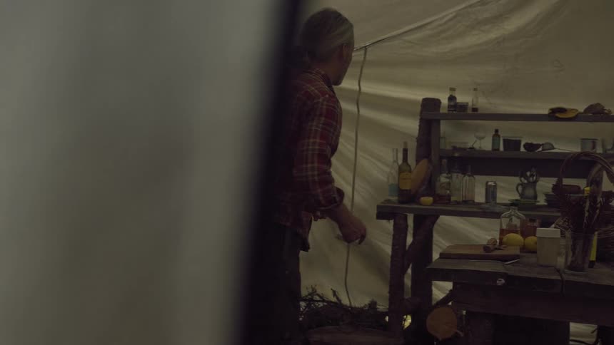 A man inside a large tent collects items from rustic furniture