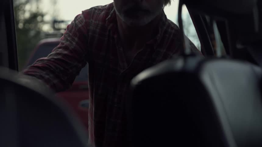 A man loads his rifle in the back seat of his vehicle