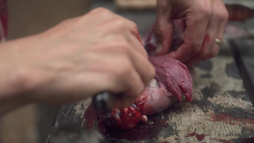 A man is trimming meat away from the ribs of a roast