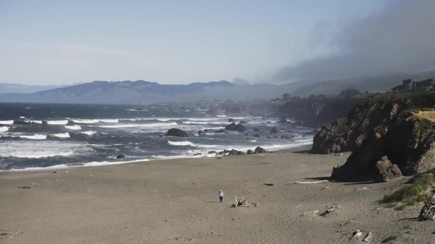 A view of the ocean and the water coming in and a person walking on the beach