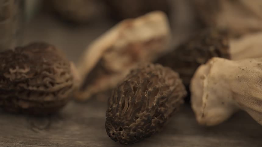 Dried morel mushrooms rest on a rustic wooden surface with the focus moving between them