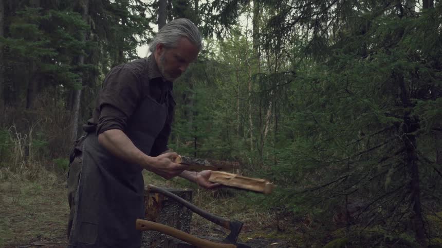 A man cuts a piece of firewood and carries it in the tent