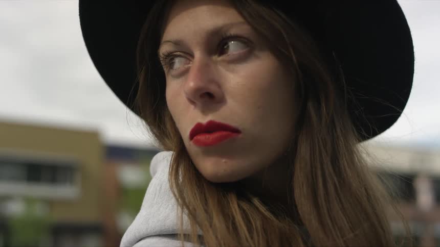 A woman wearing a hat is standing in an urban area and turning her head
