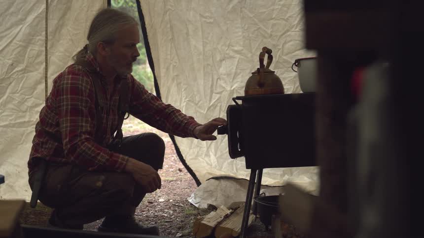 The man opens the door on the wood stove in his tent