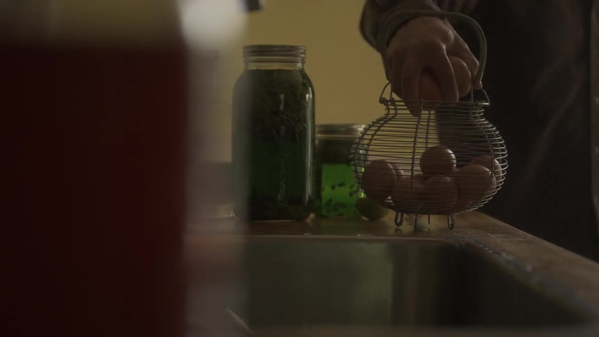 Man walking by placing fresh eggs in a wire basket sitting on the counter
