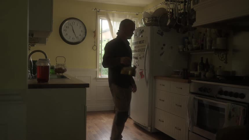A person in a dimly lit kitchen fills a teapot and places it on a stove