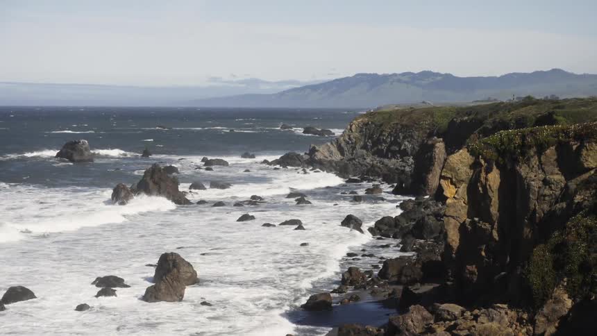 Waves are crashing over rocks below coastal cliffs
