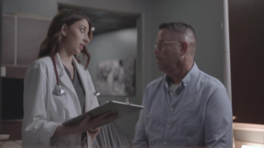 Female medical professional going over medical chart with male patient at doctors office