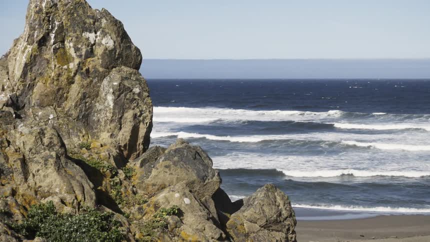 Waves roll ashore near a rock outcropping during the day