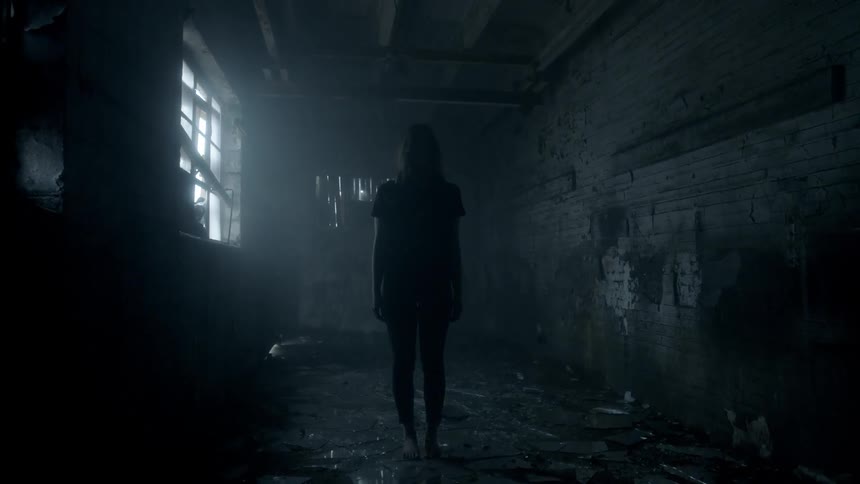A woman is standing in a dark room with only one lit window