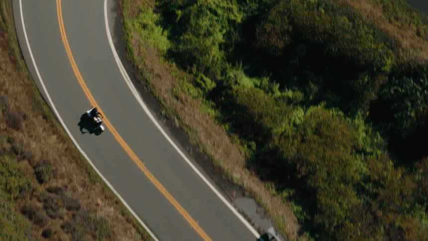 A motorcyclist navigating a winding road that cuts through a lush green landscape