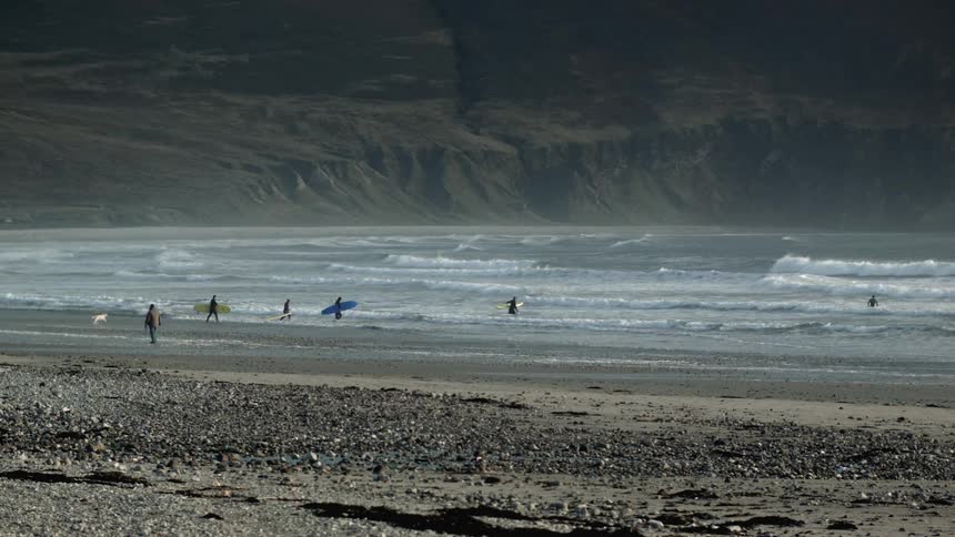 People are walking on the beach with surfboards