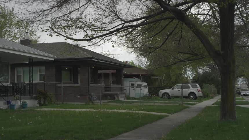 A neighborhood sidewalk has homes with cars parked