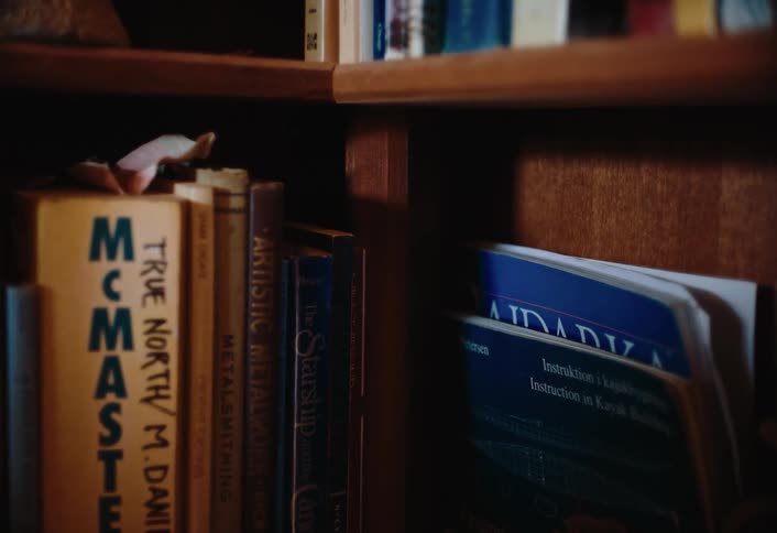 A closeup shows a section of a wooden bookshelf filled with various books stacked vertically and horizontally
