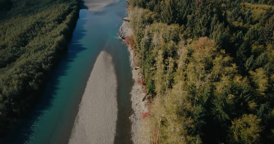 An aerial view of a winding river flowing through a lush forested valley showcasing the natural beauty of the landscape with a mix of evergreen trees and patches of sunlight illuminating the scene