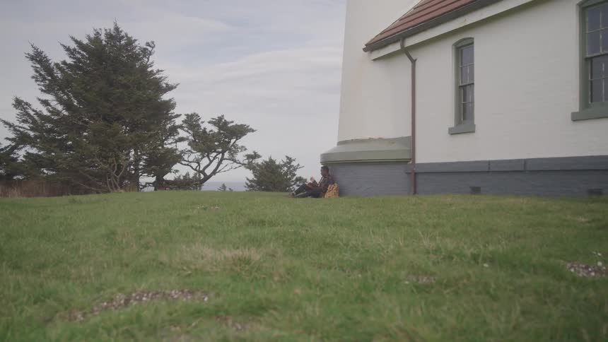 A man is sitting by the side of the home on the grass