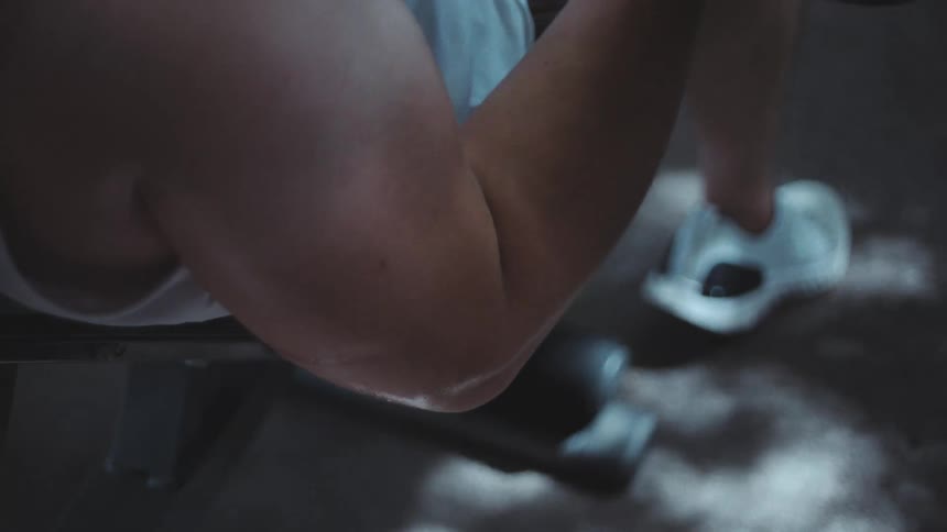 A male is lifting heavy weights while sitting at the gym