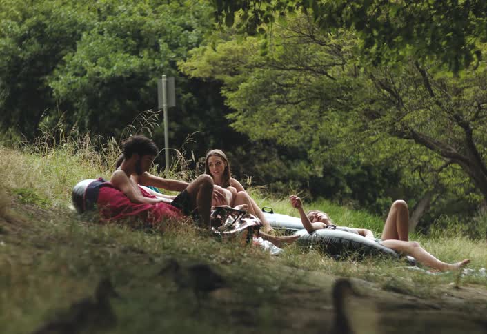 Friends lie on a slope and relax while ducks wander nearby on a summer day