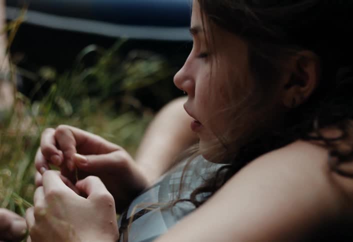 Young woman lies on an inflatable tube on the ground and tears grass while talking on a summer day