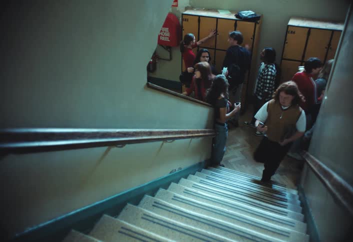 High school students rush up and down a staircase with yellow lockers lining the background