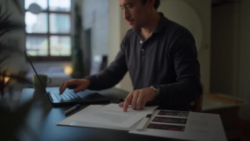 A man sits at a laptop and enters information after checking a piece of paper