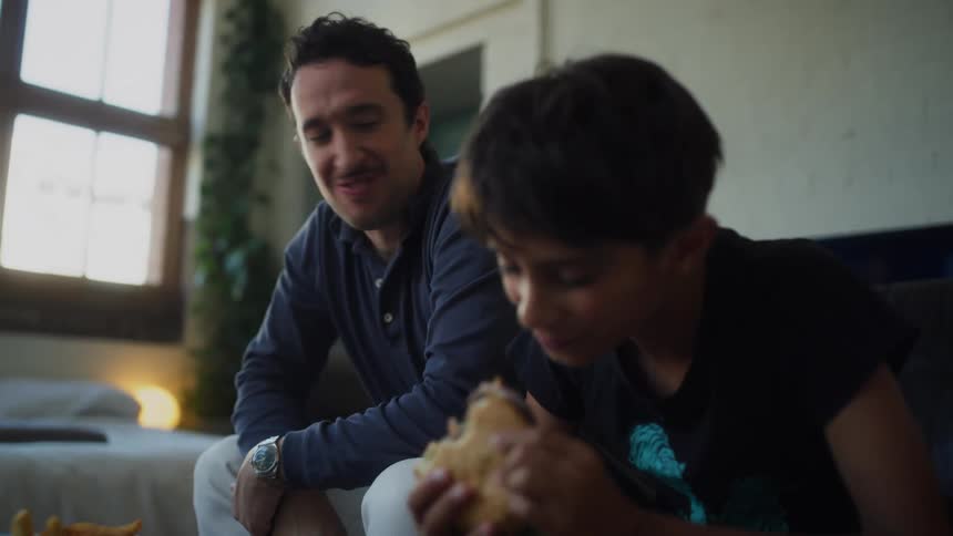 A father and son laugh as they eat a burger and fries