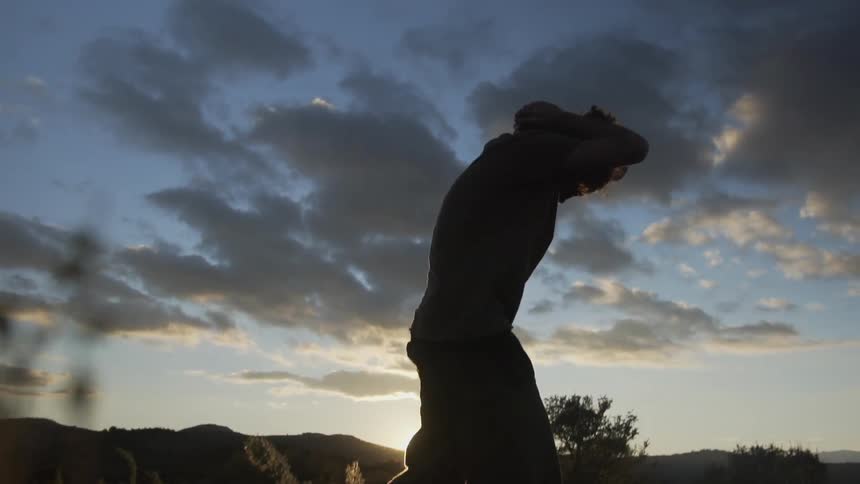 A man stands up in a field at sunset