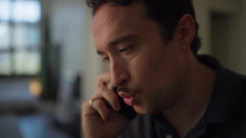 The side profile of a man with dark curly hair shows him talking on a smartphone