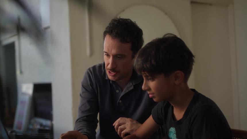 A footage of a man teaching a child on a laptop