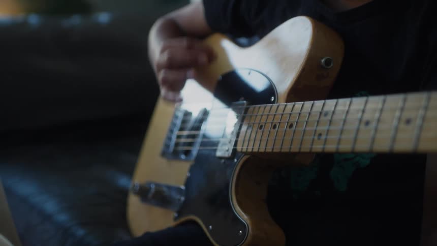 A father guiding his son on how to play an electric guitar with their hands visible on the instrument