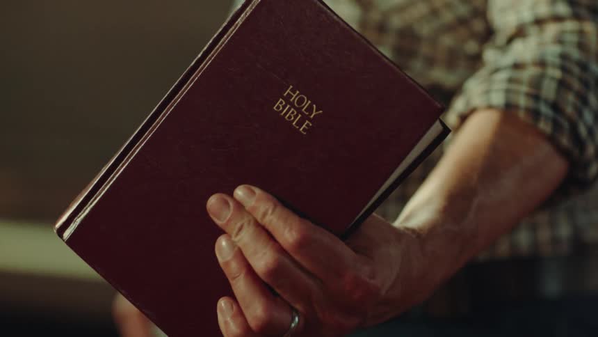 Man holds a bible in his hand facing the cover to the front