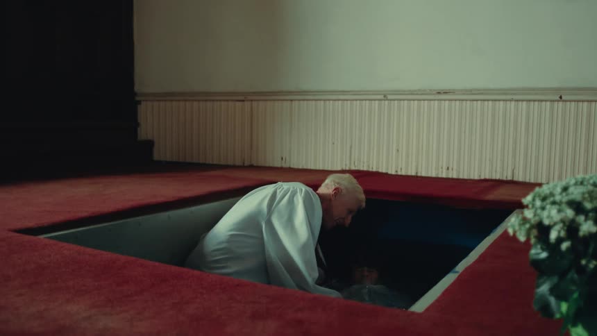 A priest baptizes a child dressed in white clothes submerging them in an underground church pool