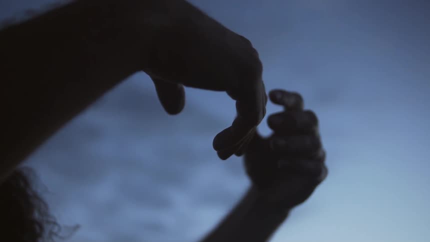 A person outstretches their hands towards the sky at dusk