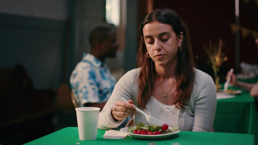 A closeup of a woman playing with food on a plate at a restaurant table looking stone faced and seemingly bored or impatient