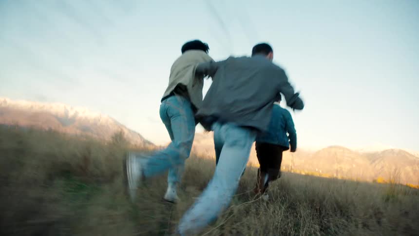 Male friends race across a field near the mountains on an autumn day
