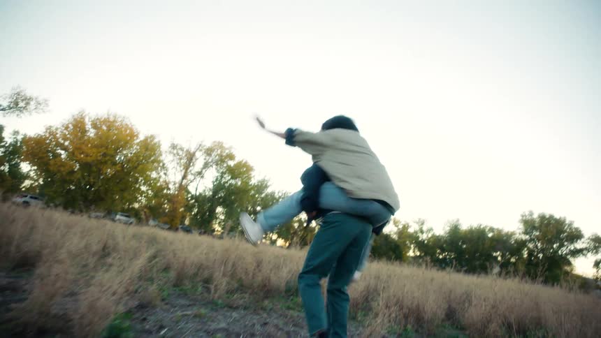 Two friends leaning on each others backs happily playing and spinning in a field
