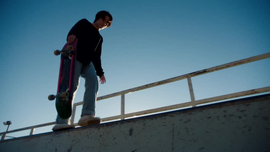 A teenager balances on the ramp with his skateboard