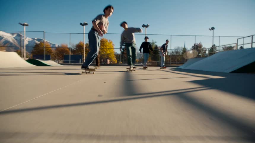 Youths skateboard at a skate park near the mountains on a sunny day