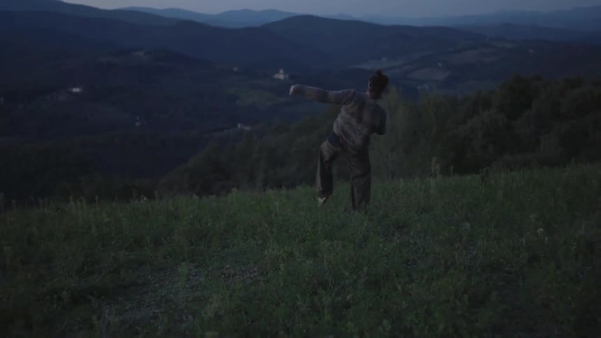 A man dancing in an open field with mountains in the background