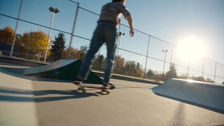 A skateboarder rides up a curved ramp in a skatepark under a bright clear sky