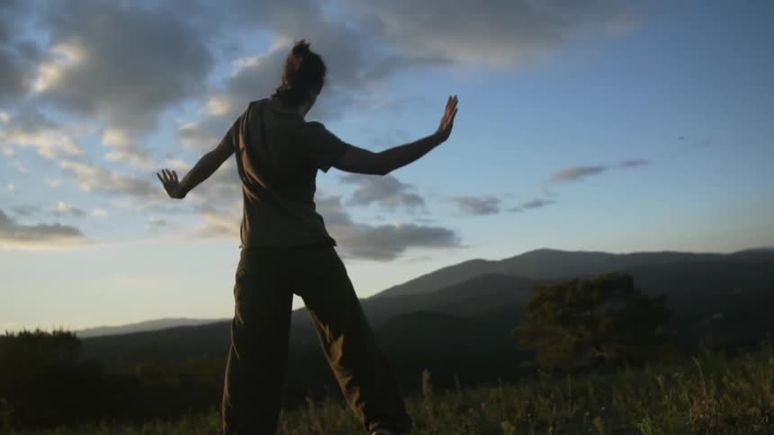 A man is dancing in the grass at sunset